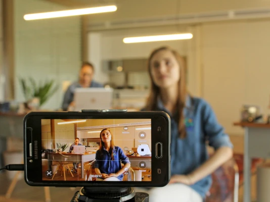 Lo schermo di un cellulare mentre riprende una ragazza in uno studio professionale. I tuoi video per il web sono uno strumento formidabile di promozione