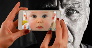 Mani di donna impugnano uno smartphone per fotografare un uomo anziano, ma nello schermo si vede invece un bambino